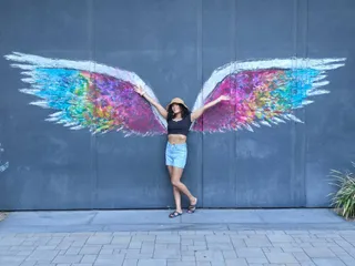 Euri posing in front of a colorful angel wings mural