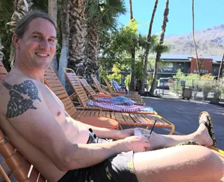 Jereme on a pool lounger with a drink, the mountains behind him