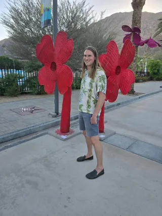 Jereme standing between two giant red woven flower sculptures