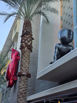 A red car mounted on a building wall next to a giant baby sculpture on a ledge
