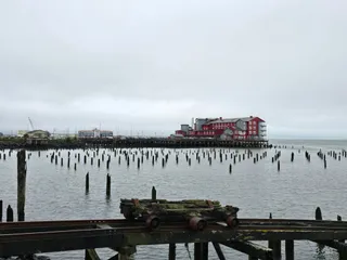 Rows of old pilings in the river, with the red Cannery Pier Hotel in the distance