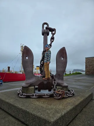 Jereme standing inside a giant anchor, with the red Lightship Columbia behind him