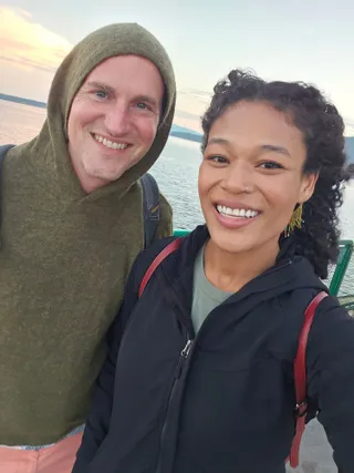 Jereme in his hood and Euri smiling on the ferry deck at sunset