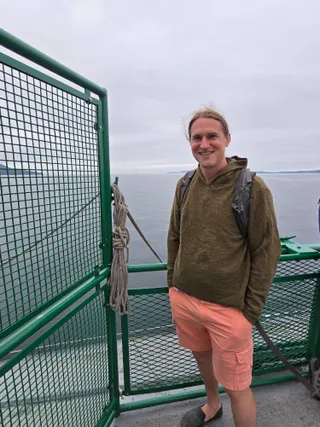 Jereme on the outer deck of a Washington State ferry, with gray water and islands behind him