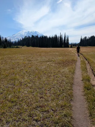 Jereme walking ahead on the trail through the meadow toward Mount Rainier